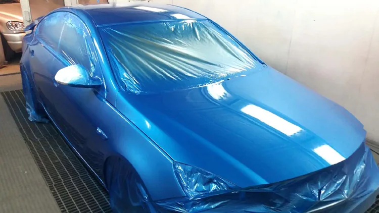 Vehículo azul metalizado dentro de la cabina de pintura