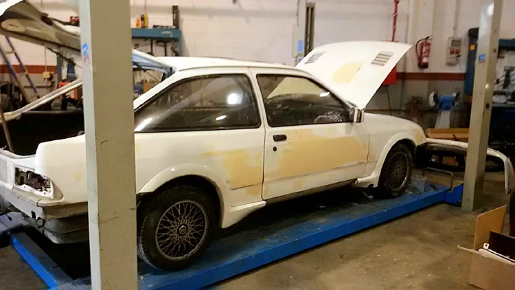 Ford Sierra Cosworth blanco en la bancada del taller, con el capó abierto