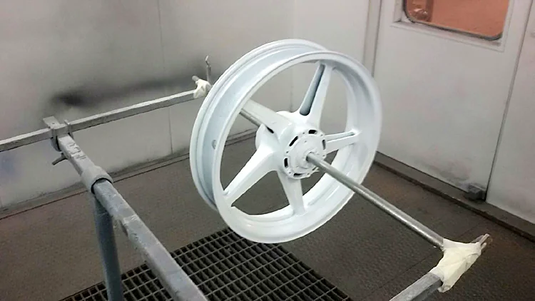 Llanta de moto pintada en blanco colgada en la cabina de pintura