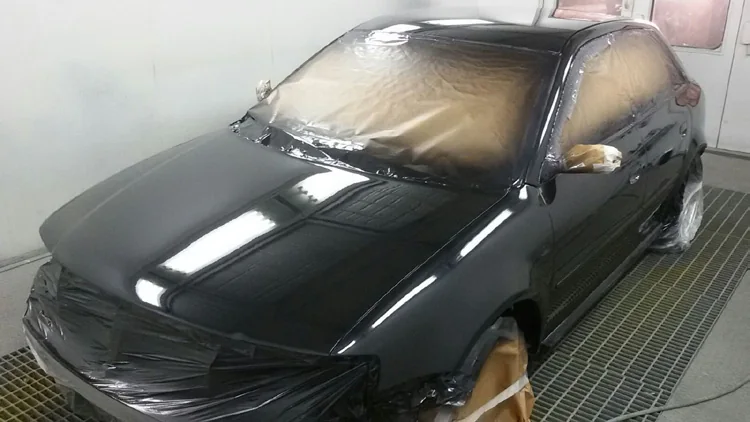 Coche negro brillante dentro de la cabina de pintura